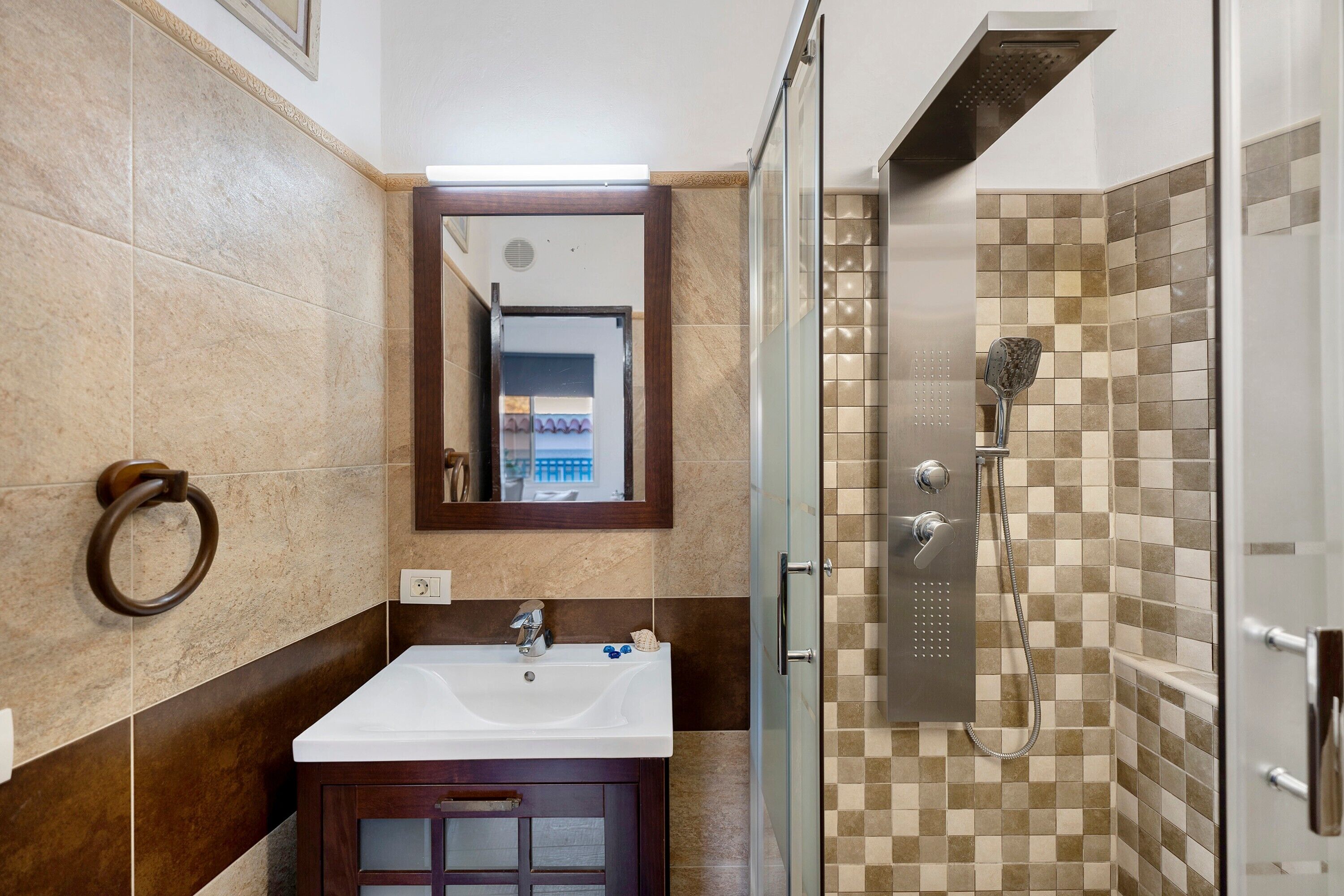 A bathroom with a sink, mirror, towel ring, shower, and tiled walls.