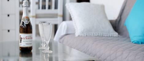 Eine Flasche Sidra El Gaiter auf einem Tisch mit einem klaren Glas daneben, in einem Zimmer mit einem Bett und weißen Möbeln.
