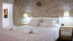 Un dormitorio con pared de piedra, una cama con ropa de cama floral, dos lámparas de noche y una mesita de noche con un reloj.