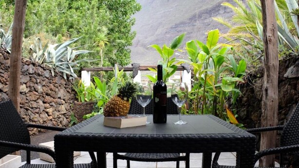 Un área de comedor al aire libre con una mesa, sillas, una botella de vino y una piña.