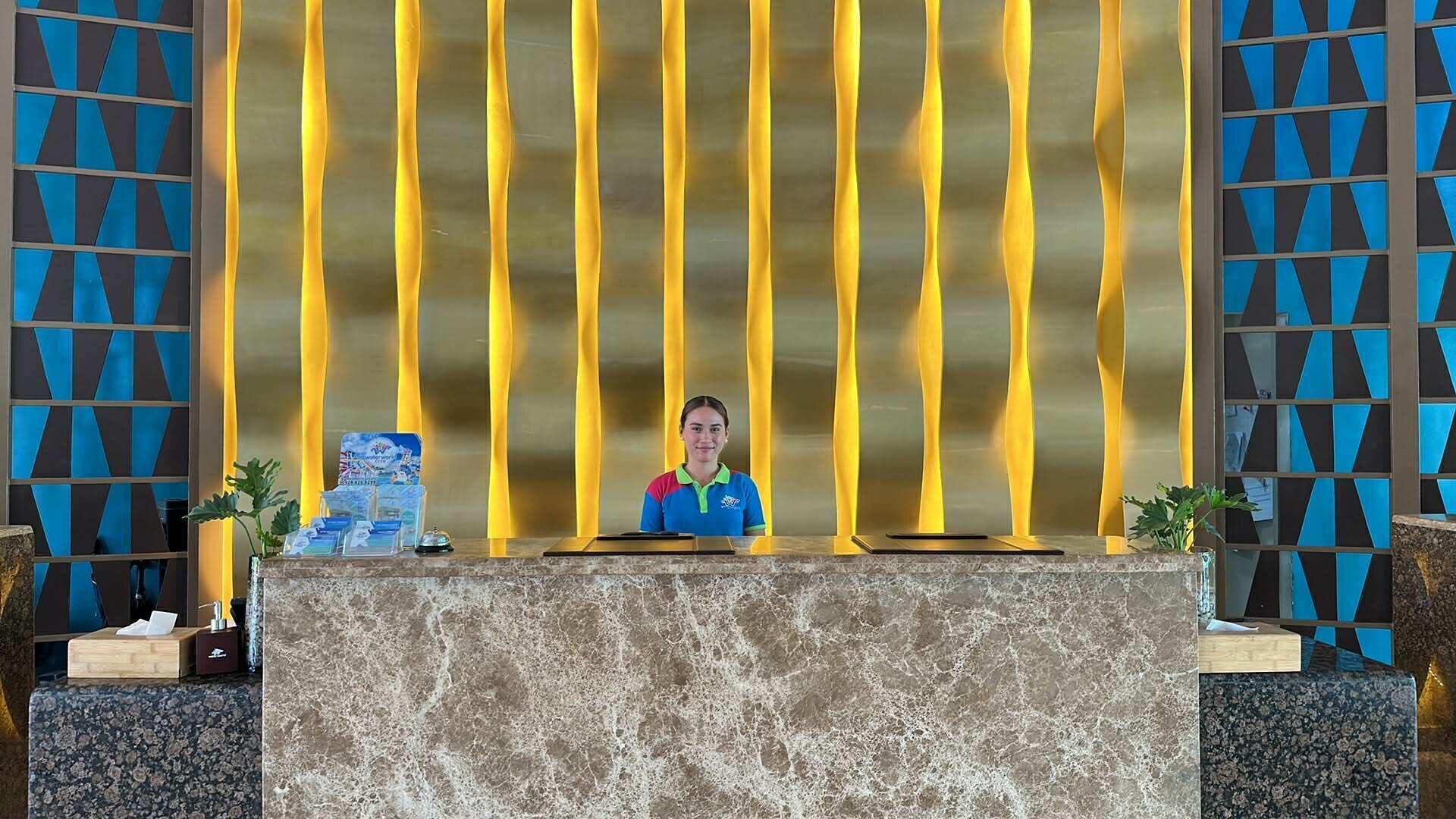 Un mostrador de recepción con encimera de mármol, una recepcionista y una pared con estampado azul y negro.