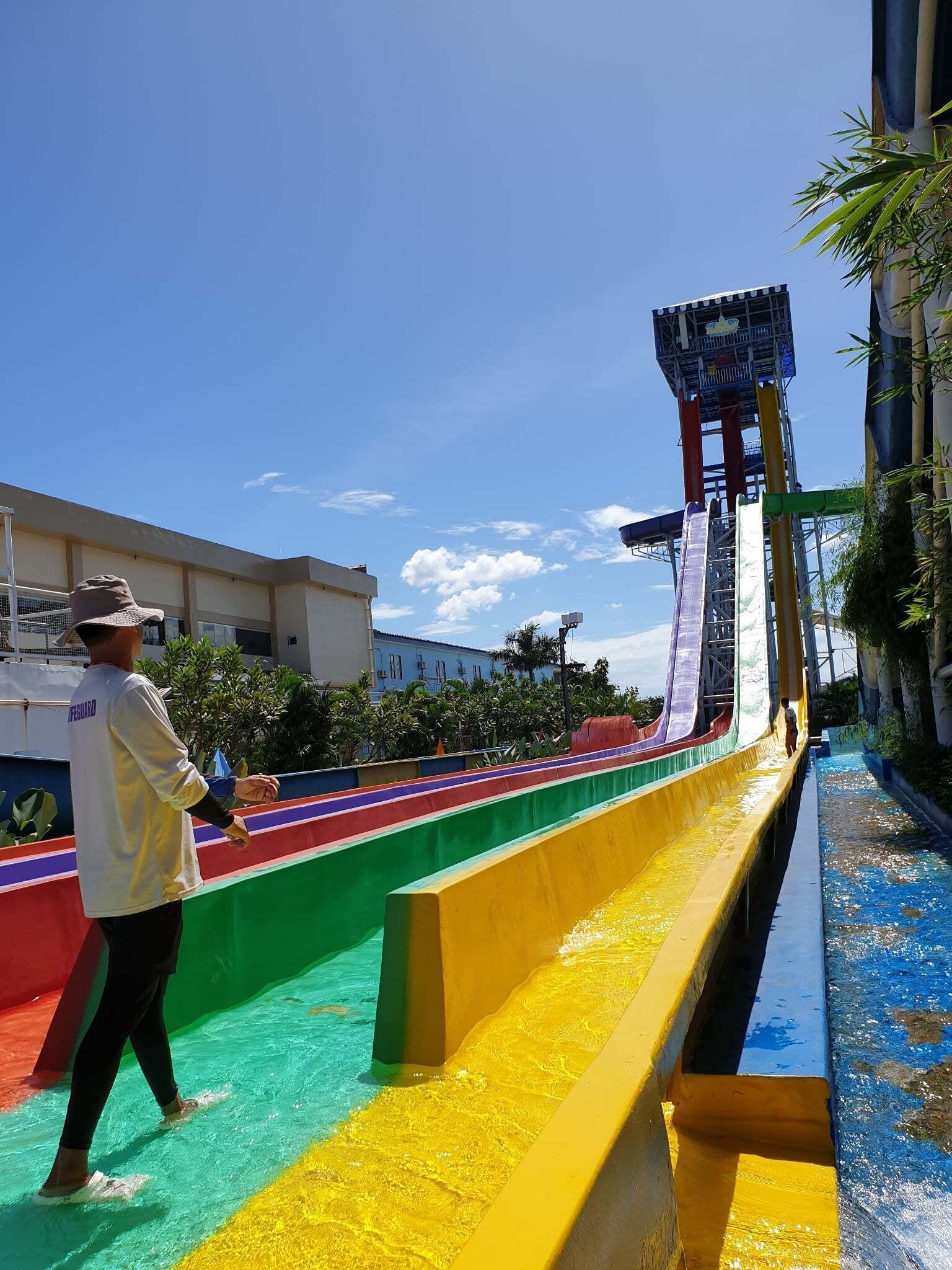 A water slide with a person at the bottom, a lifeguard, and a building in the background.