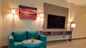 Una sala de estar con un sofá color turquesa, una mesa redonda de centro, un televisor de pantalla plana montado en la pared y dos lámparas de pared.