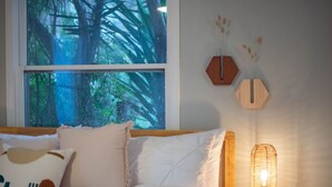 A bedroom with a large window, a bed with white bedding, two hexagonal wall decorations, and a table lamp. - Pt Loma Paradise: Remodel - Pool – Game Room – WOW! (San Diego)