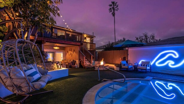 A pool area with a neon wave design, a swing chair, and a wooden deck. - Pt Loma Paradise: Remodel - Pool – Game Room – WOW! (San Diego)