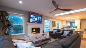 A modern living room with a fireplace, a flat-screen TV, and a ceiling fan. - Pt Loma Paradise: Remodel - Pool – Game Room – WOW! (San Diego)