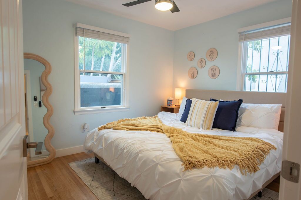 A bedroom with a bed, a mirror, a window, and wall decor.