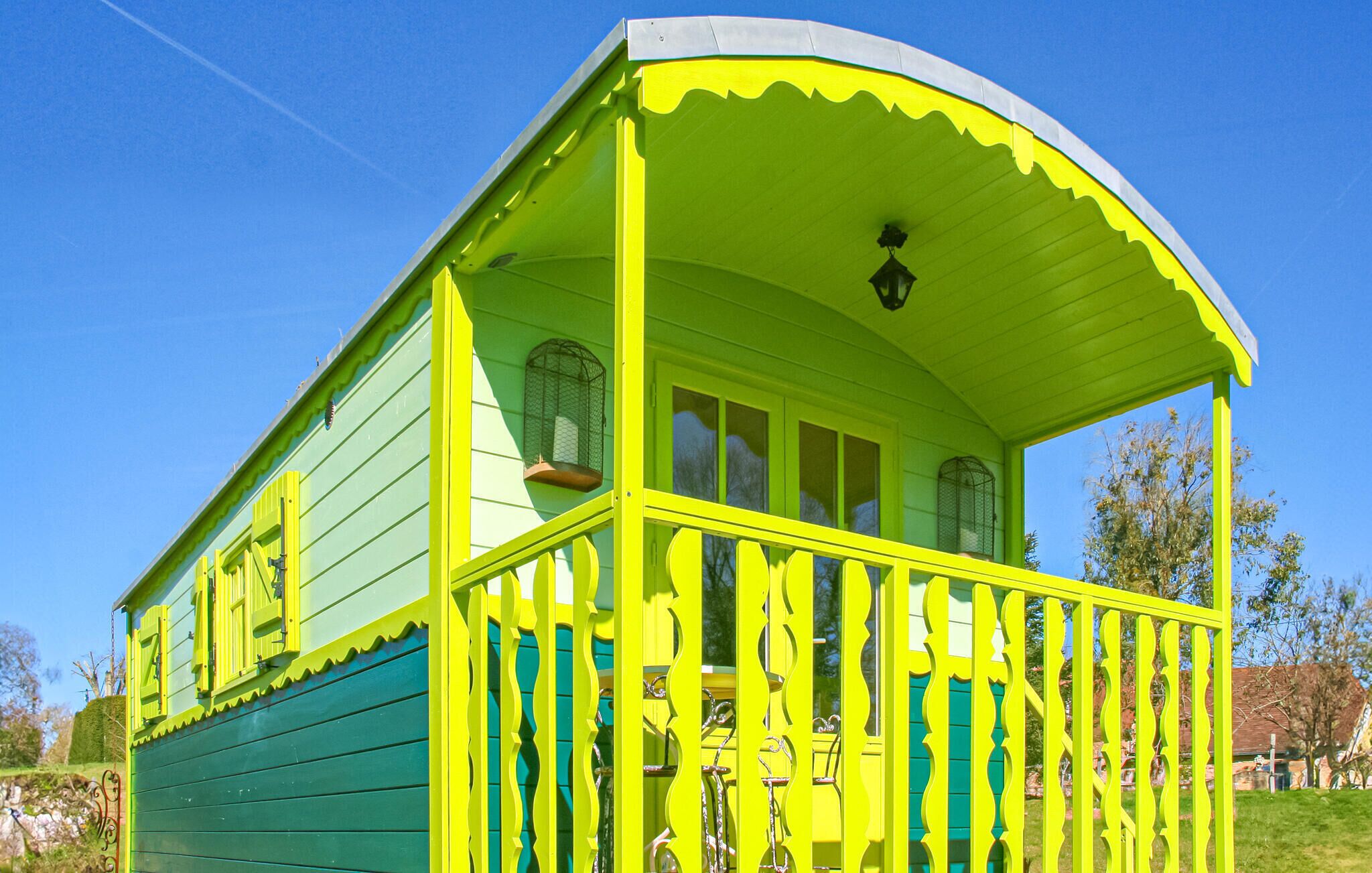 A small, single-story building with a green exterior and yellow accents, featuring a balcony with a curved roof and a small porch area.