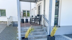 Een modern gebouw met een overdekt terras, een trap naar een deur en twee potplanten op de grond.