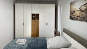 Een slaapkamer met een bed, een kledingkast, een klein houten plankje en een aan de muur hangend schilderij.
