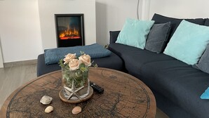 Een woonkamer met een open haard, een ronde salontafel met decoratieve objecten, een bank met blauwe kussens en een lamp.