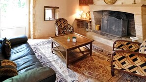 Ein gemütliches Wohnzimmer mit Kamin, einer Couch, einem gemusterten Sessel und einem Couchtisch.