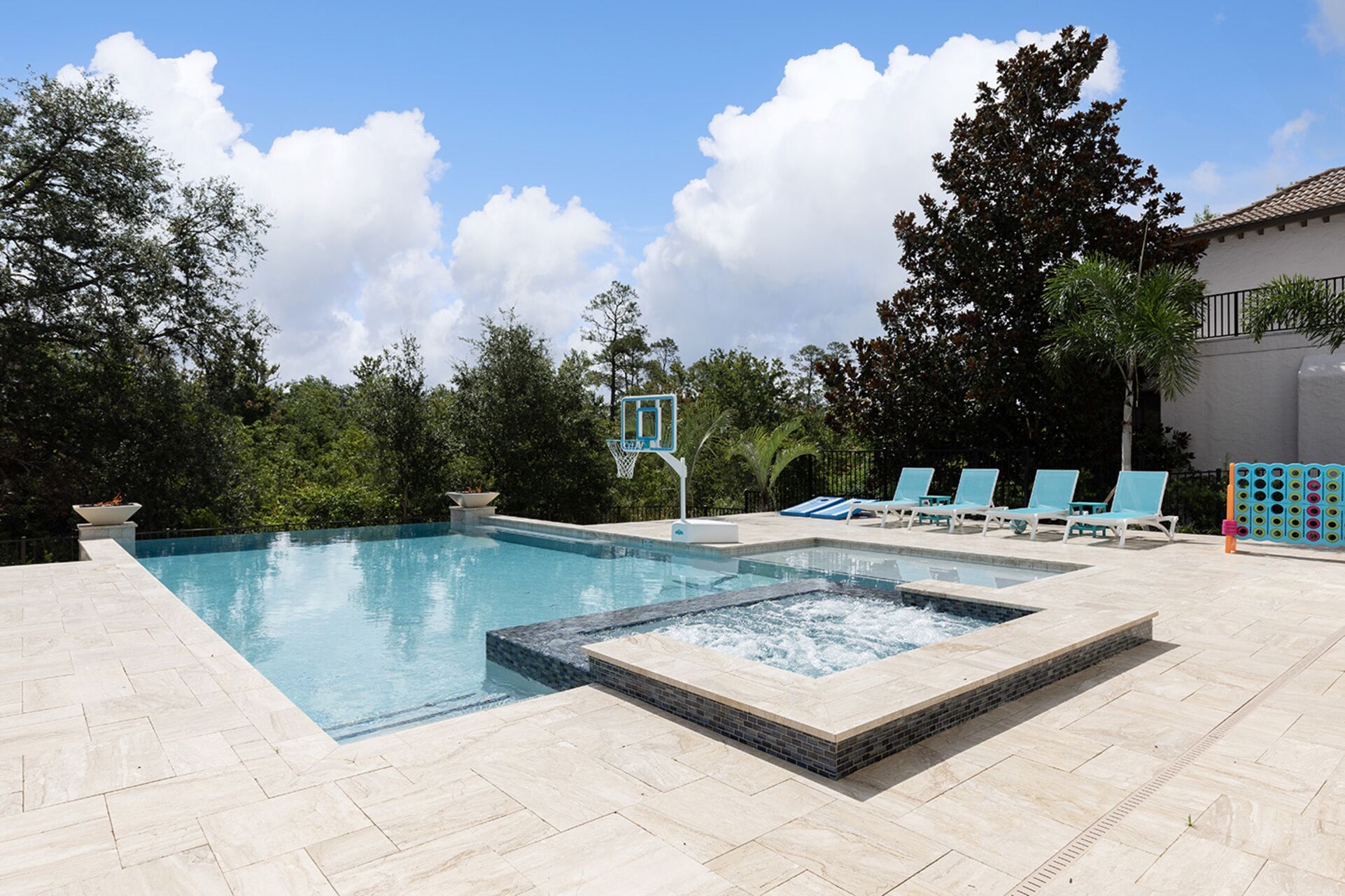 A swimming pool with a hot tub, lounge chairs, and a basketball hoop.