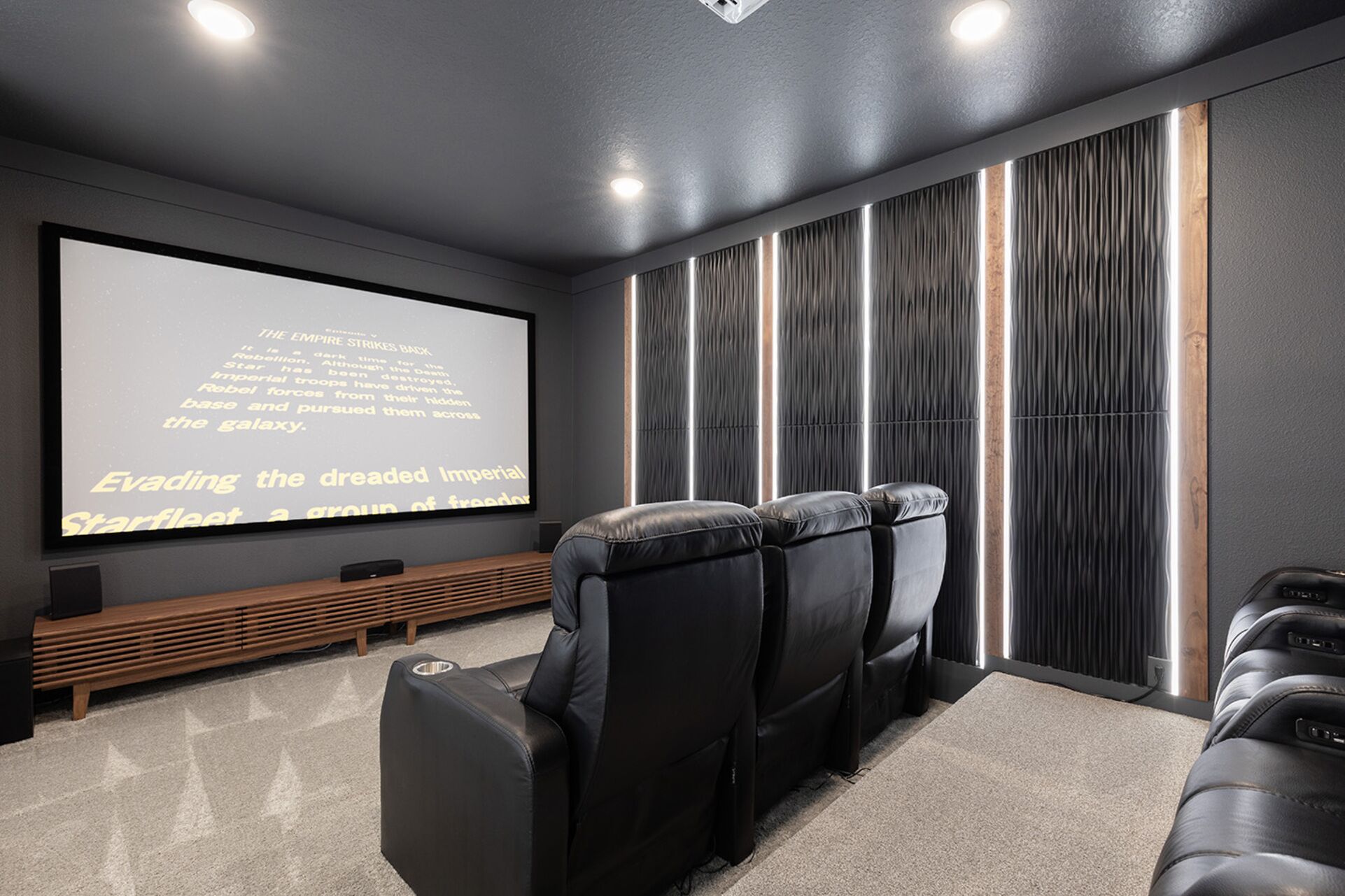 Un home theater con un grande schermo, poltrone in pelle reclinabili e una panca in legno.