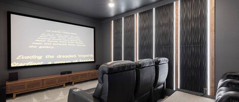 Un home theater con un grande schermo, poltrone in pelle reclinabili e una panca in legno.