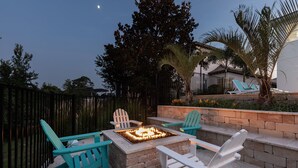 An outdoor patio with Adirondack chairs, a stone fire pit, and a view of a house and palm trees. - Beautiful Villa with First Class Amenities in Reunion Resort, Orlando Villa 1011 (Orlando)