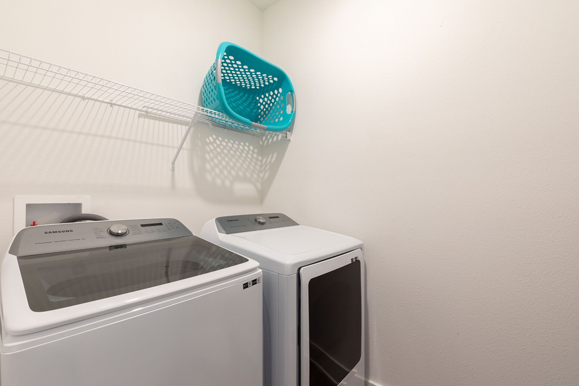 A laundry area with two washing machines and a blue laundry basket on a white wall.
