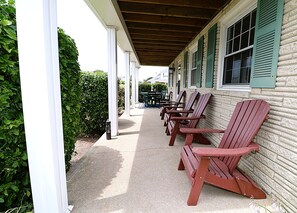 A covered porch with Adirondack chairs lined up against a brick wall. - Reel 'em Inn - Newly Renovated Kitchen & Baths (Brigantine)