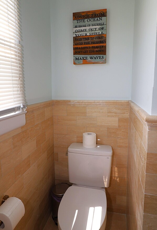 Un baño con inodoro, rollo de papel higiénico y un cubo de basura.