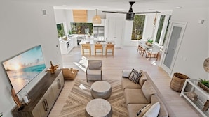 A modern living room with a sofa, coffee table, and TV. There is a kitchen in the background with a dining area. - Luxury Retreat w/Games, Patio, BBQ, Close to Beach (Palm Coast)