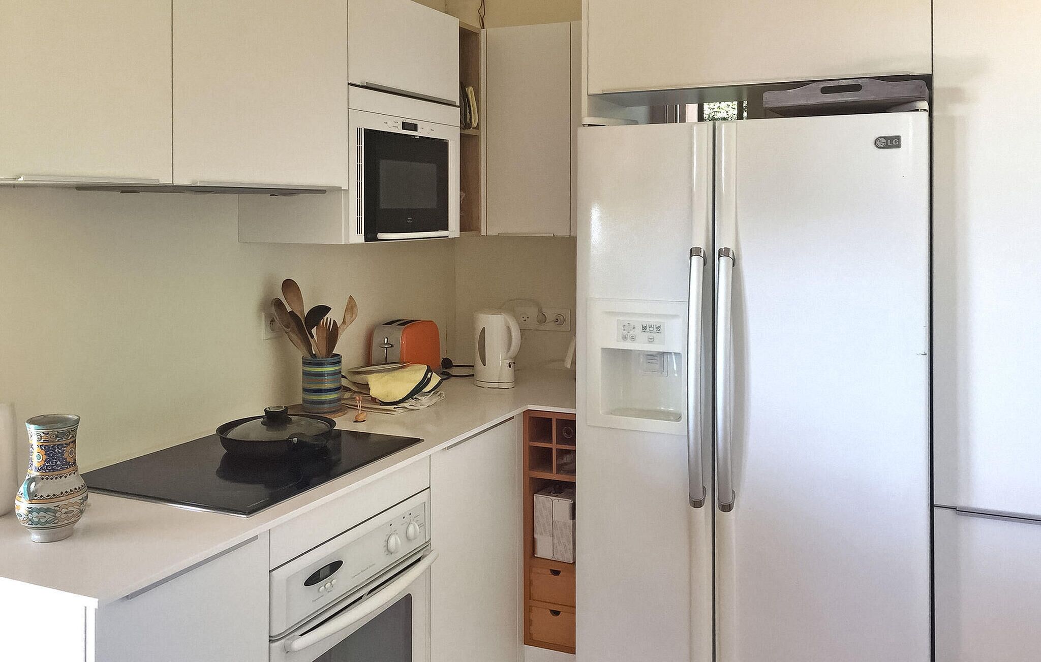 A compact kitchen with a microwave, a toaster, a kettle, and a refrigerator.