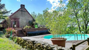 Una casa de piedra rústica con techo de paja, una terraza de madera y una piscina.