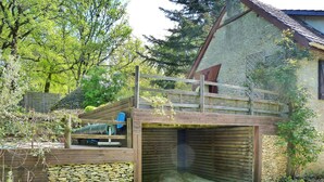 Una cabaña rústica con terraza de madera y paredes de piedra, rodeada de exuberante vegetación.