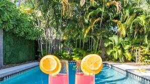 A poolside setting with two drinks, sunglasses, and an orange slice on a tray. - Tranquil Oasis: Newly Renovated Villa, Heated Pool, Private Garden Retreat (Fort Lauderdale)