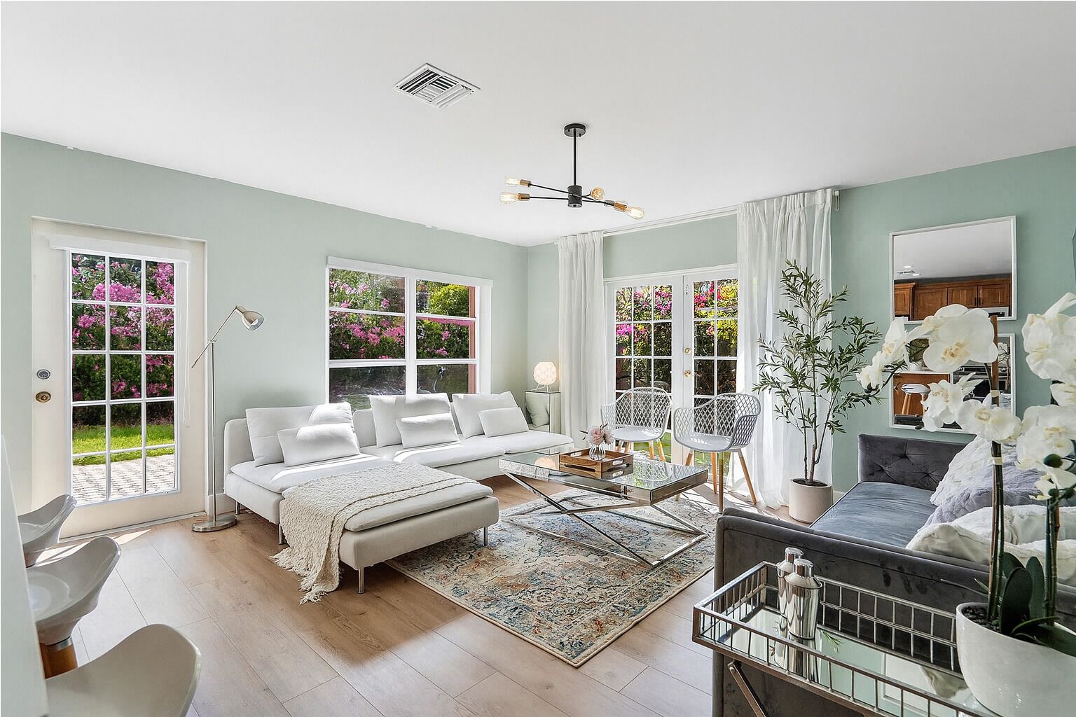 Un salon moderne comprenant un canapé, des fauteuils, une table basse et une grande fenêtre donnant sur un paysage verdoyant.