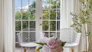 A room with a glass table, two white wireframe chairs, a vase with a pink flower, and a potted plant. - Tranquil Oasis: Newly Renovated Villa, Heated Pool, Private Garden Retreat (Fort Lauderdale)
