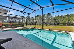 A covered outdoor swimming pool with a hot tub, lounge chairs, and a view of a building and trees. - Paradise Palms Resort 6 Bedroom Private Pool+Spa Home (Kissimmee)