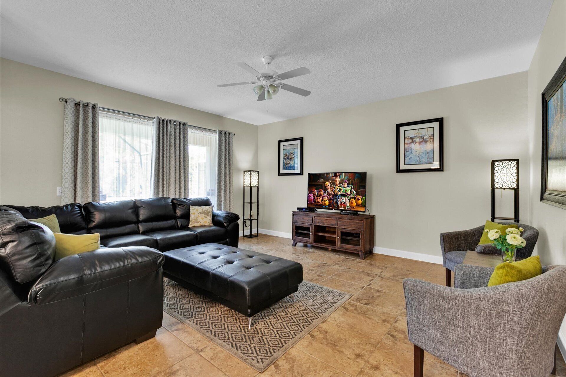 A living room with a black leather sofa, a grey armchair, a wooden TV stand, and a ceiling fan.