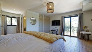 Un dormitorio con una cama grande, una lámpara en el techo, un televisor y un balcón con una silla y una planta.