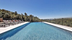 Una piscina rectangular con agua azul cristalina, rodeada por una cerca de metal y una fila de tumbonas a un lado.