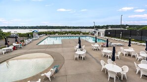 Un espace piscine avec des chaises longues et des parasols, une petite piscine, et une vue sur l’eau et les bateaux au loin.