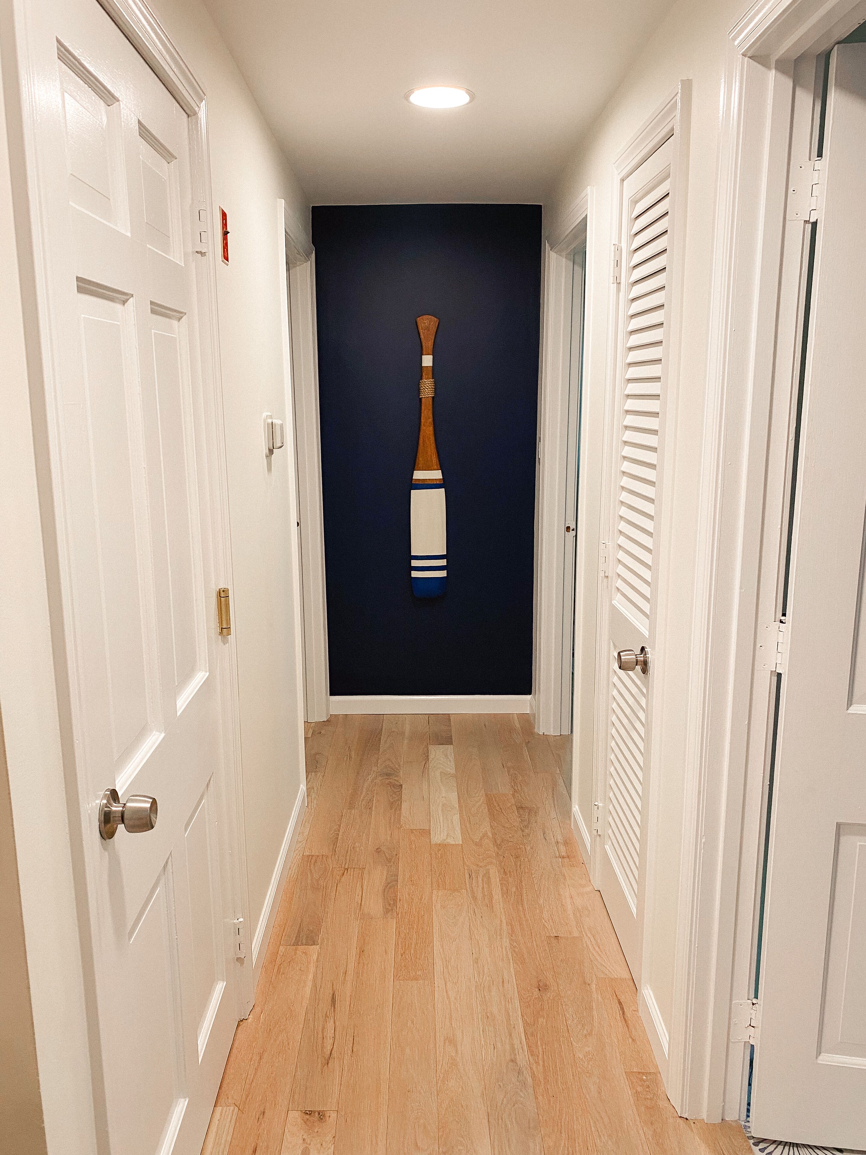 A hallway with wooden flooring, white doors, and a dark blue wall with a wooden bat decoration.