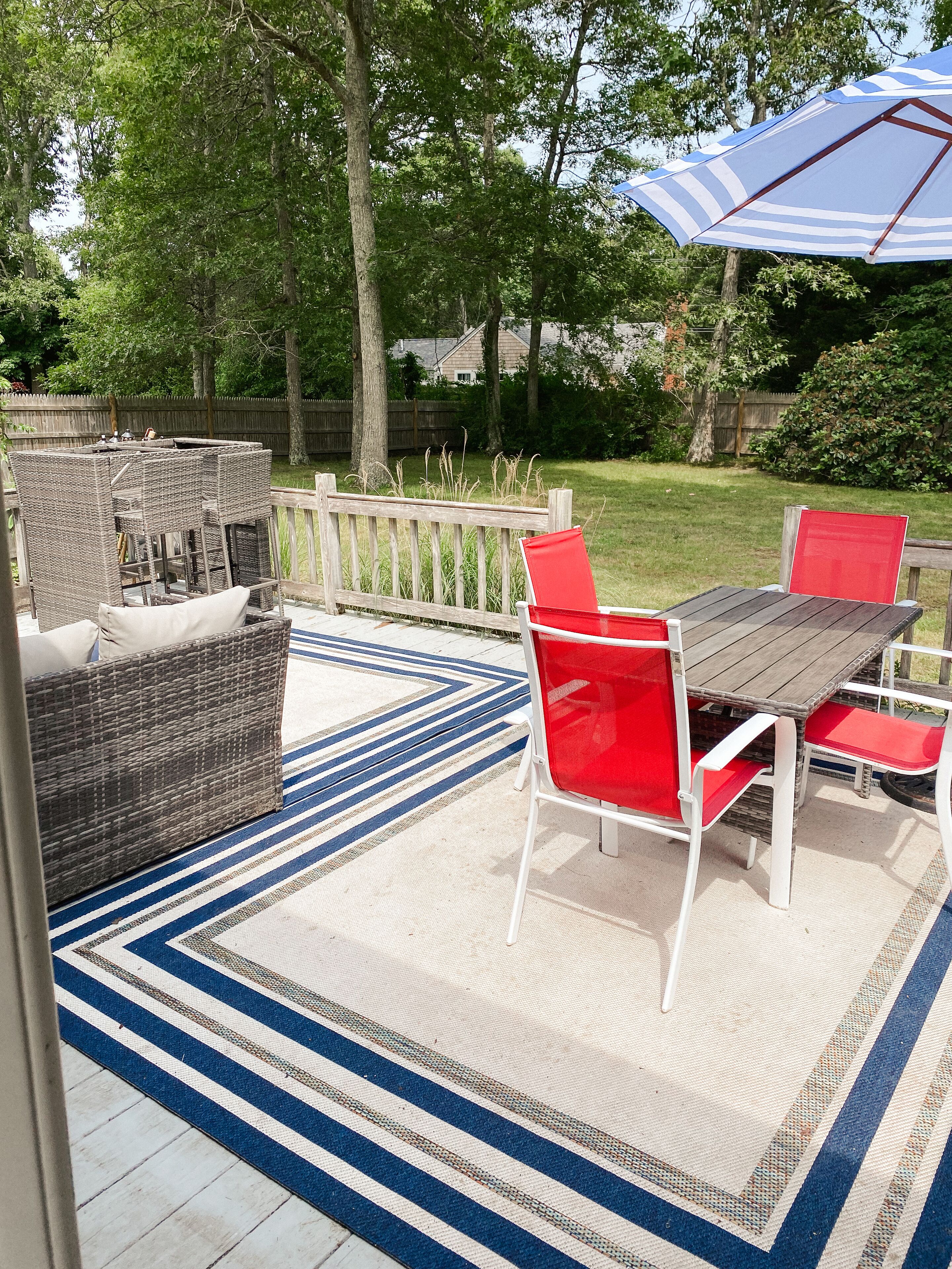 An outdoor patio with wicker furniture, a wooden table, and red chairs.