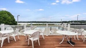 Une terrasse extérieure avec des tables et des chaises blanches, une piscine en arrière-plan et une vue sur le paysage.