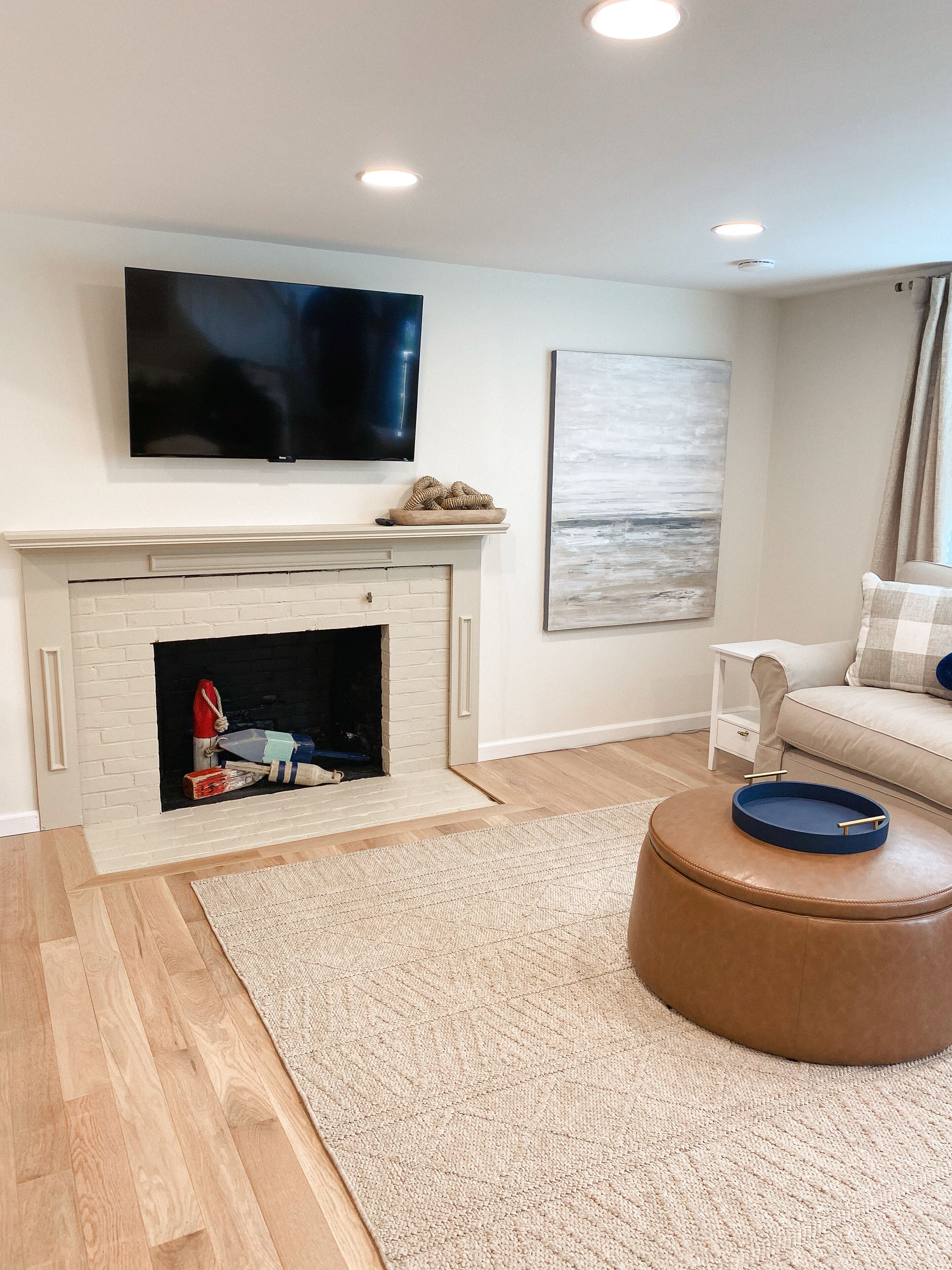 Una sala de estar moderna con chimenea, un televisor de pantalla plana montado encima, un sofá beige y un otoman marrón con una bandeja.