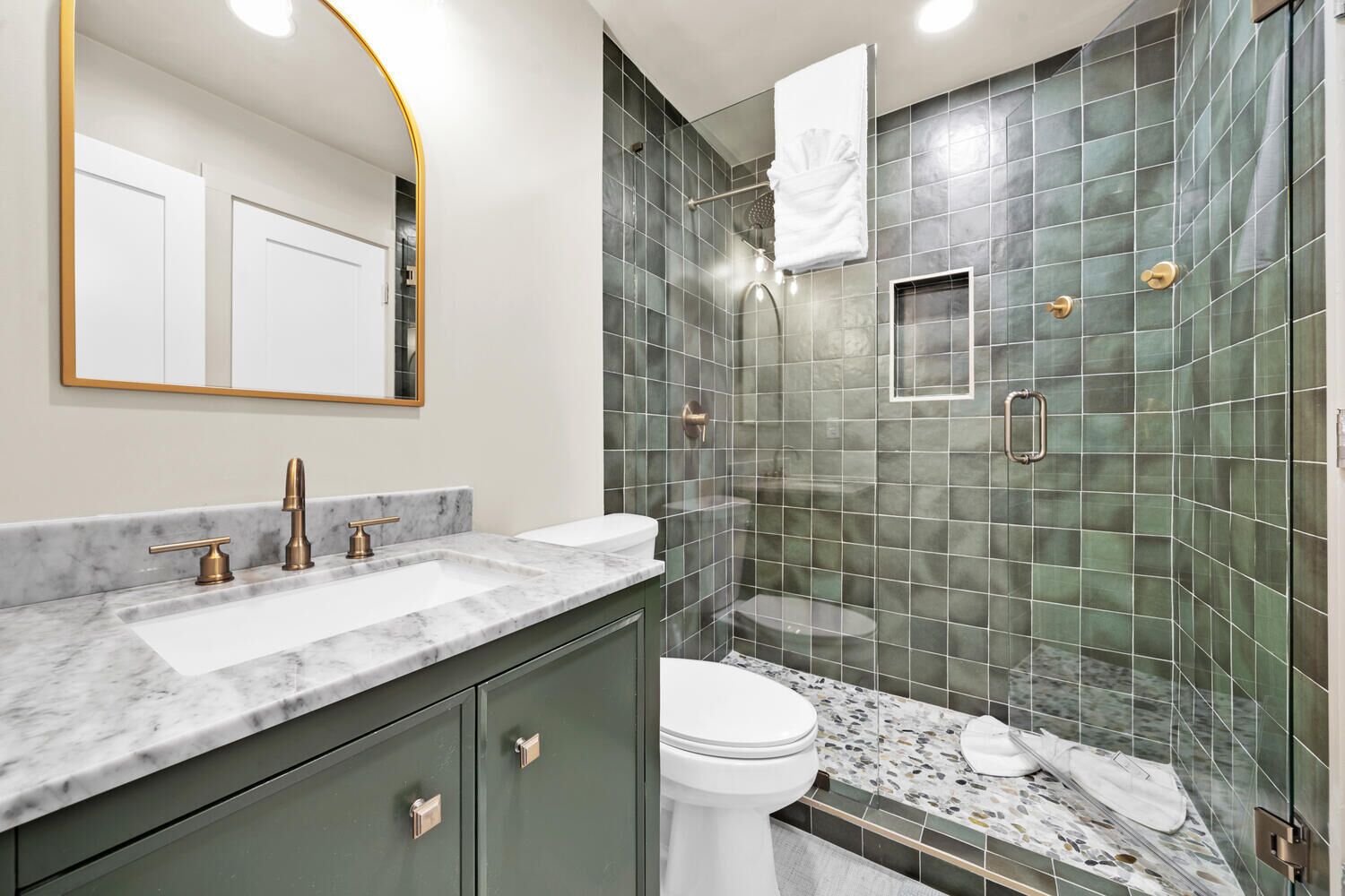 A modern bathroom with a marble sink, a toilet, and a shower with green tiles.
