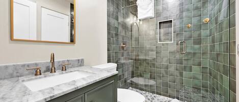 A modern bathroom with a marble sink, a toilet, and a shower with green tiles.