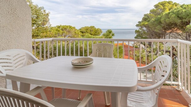 Ein weißer Tisch und Stühle auf einem Balkon mit Blick auf das Meer und Bäume.