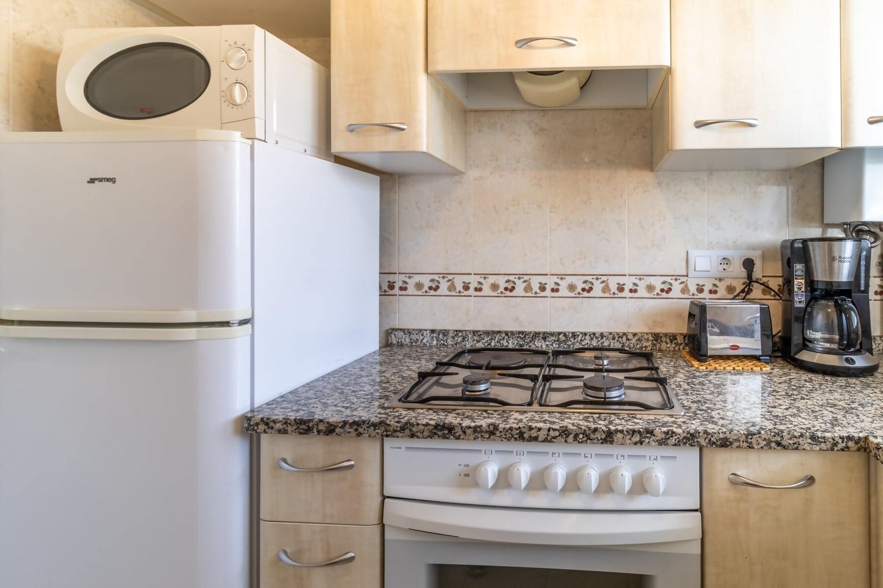 Une cuisine de taille réduite, équipée d’un réfrigérateur blanc, d’une cuisinière à gaz, d’un grille-pain et d’une machine à café.