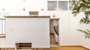 Un edificio blanco con base de piedra, una ventana pequeña y una puerta que da a una escalera.