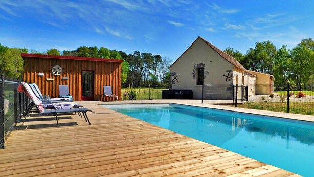 Een houten terras met lounge fauteuils, een zwembad en twee gebouwen met verschillende architectuur.