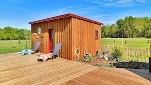 Een houten chalet met een rood dak, een deur en een klein Amerikaans vlaggetje. Er staan twee ligstoelen met handdoeken op een houten terras voor het chalet.