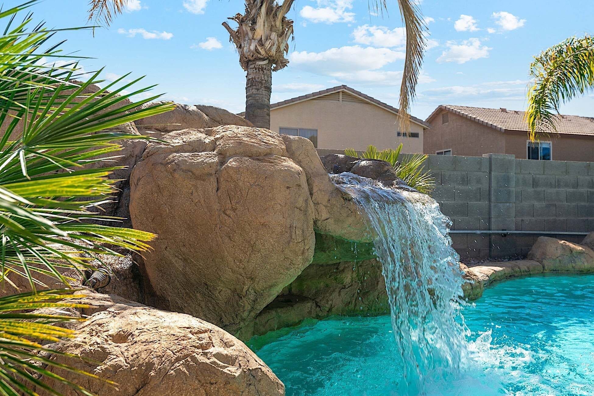 A pool with a waterfall feature, surrounded by rocks and palm trees.