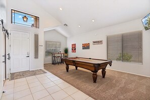 Una habitación amplia con mesa de billar, una puerta con ventana y un cartel en la pared.