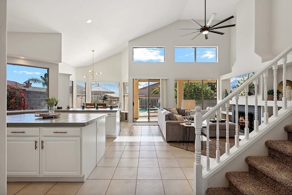 A spacious kitchen with a central island, a dining area with a sofa, and a staircase leading to a living area.