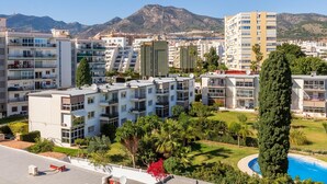 Un quartier résidentiel avec des immeubles d’appartements modernes, une piscine et un paysage montagneux en toile de fond.